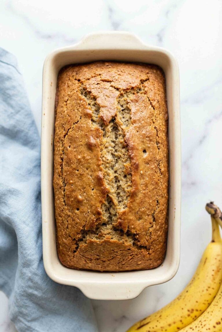 Golden brown almond flour banana bread baked in a white ceramic dish with naturally cracked top and caramelized edges