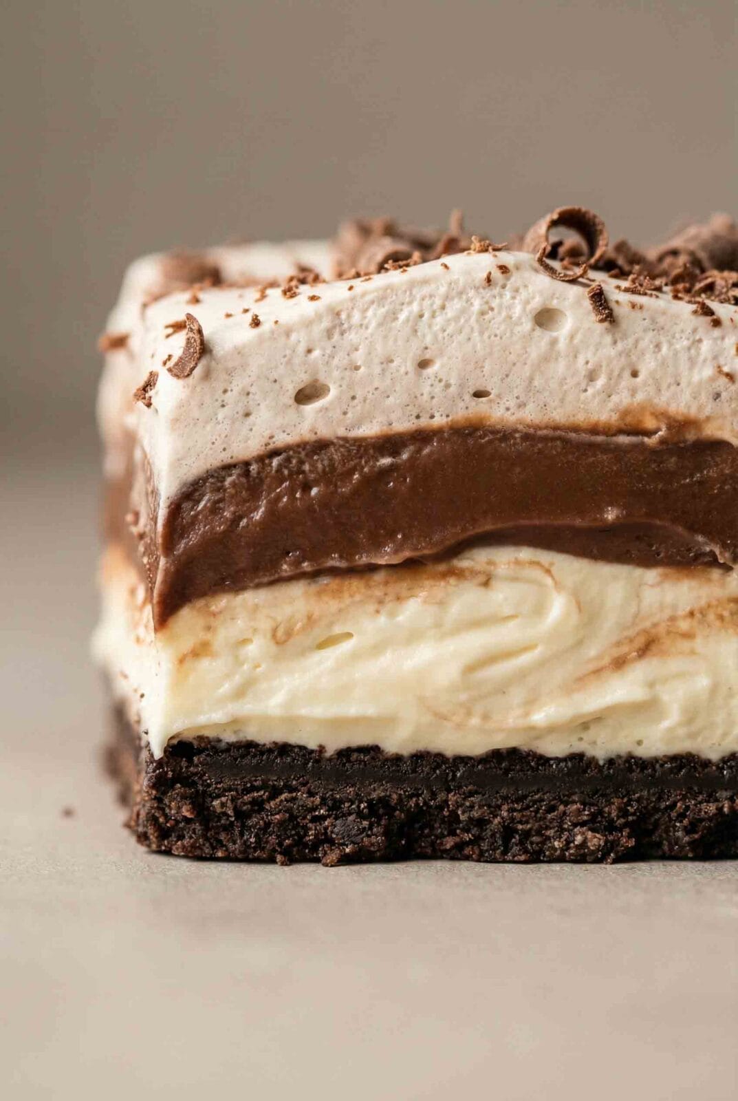 Close-up of Chocolate Lasagna (No-Bake) showing cookie crumb crust, smooth cream, rich chocolate pudding layers, and whipped topping