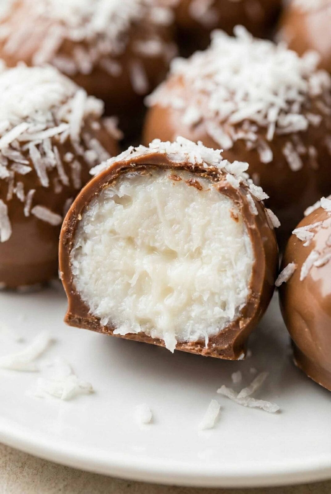 Ultra-close view of chocolate coconut truffles cut open, revealing dense white coconut filling inside a smooth milk chocolate shell
