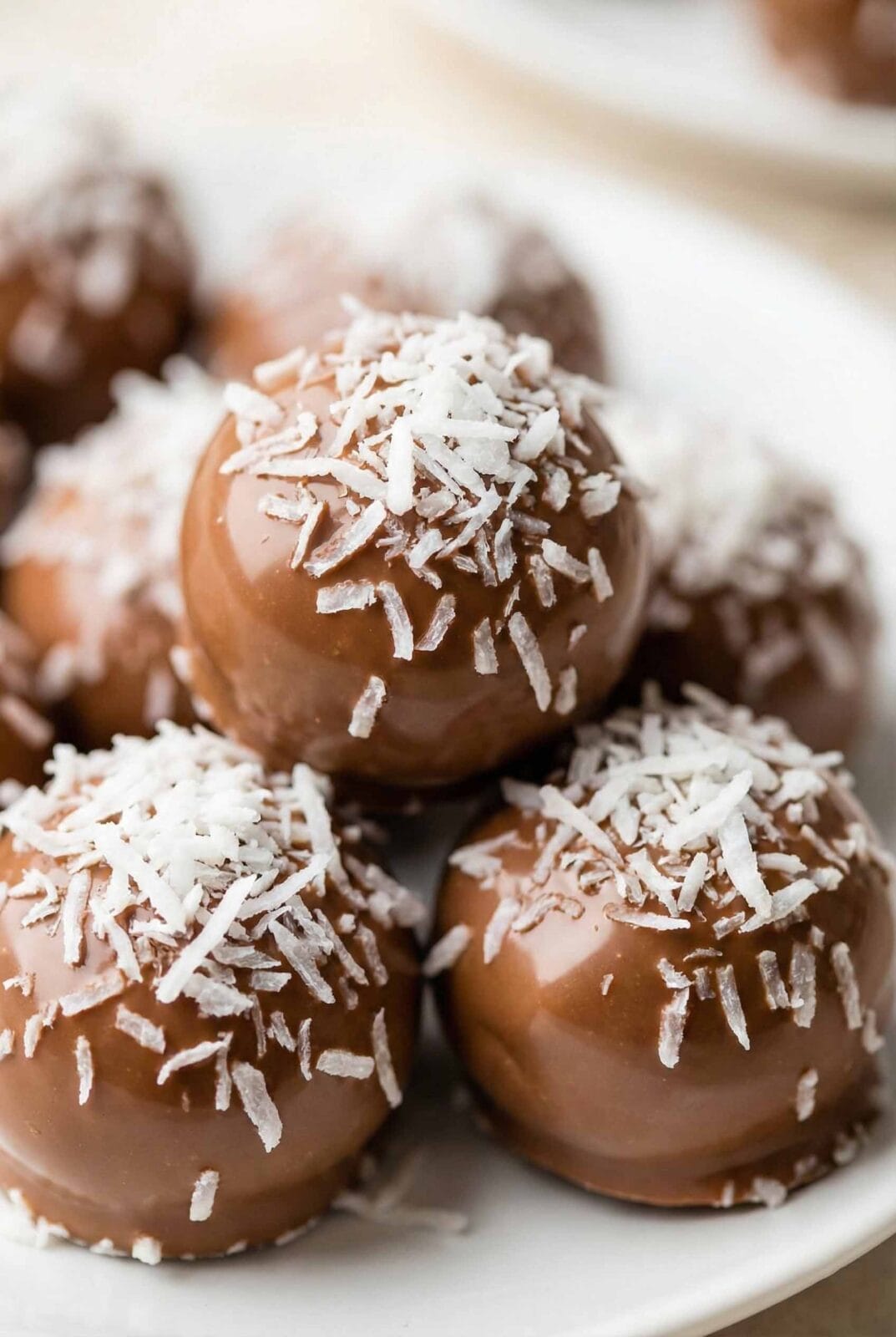 Extreme macro of chocolate coconut truffles clustered tightly, topped with bright white shredded coconut on glossy milk chocolate shells