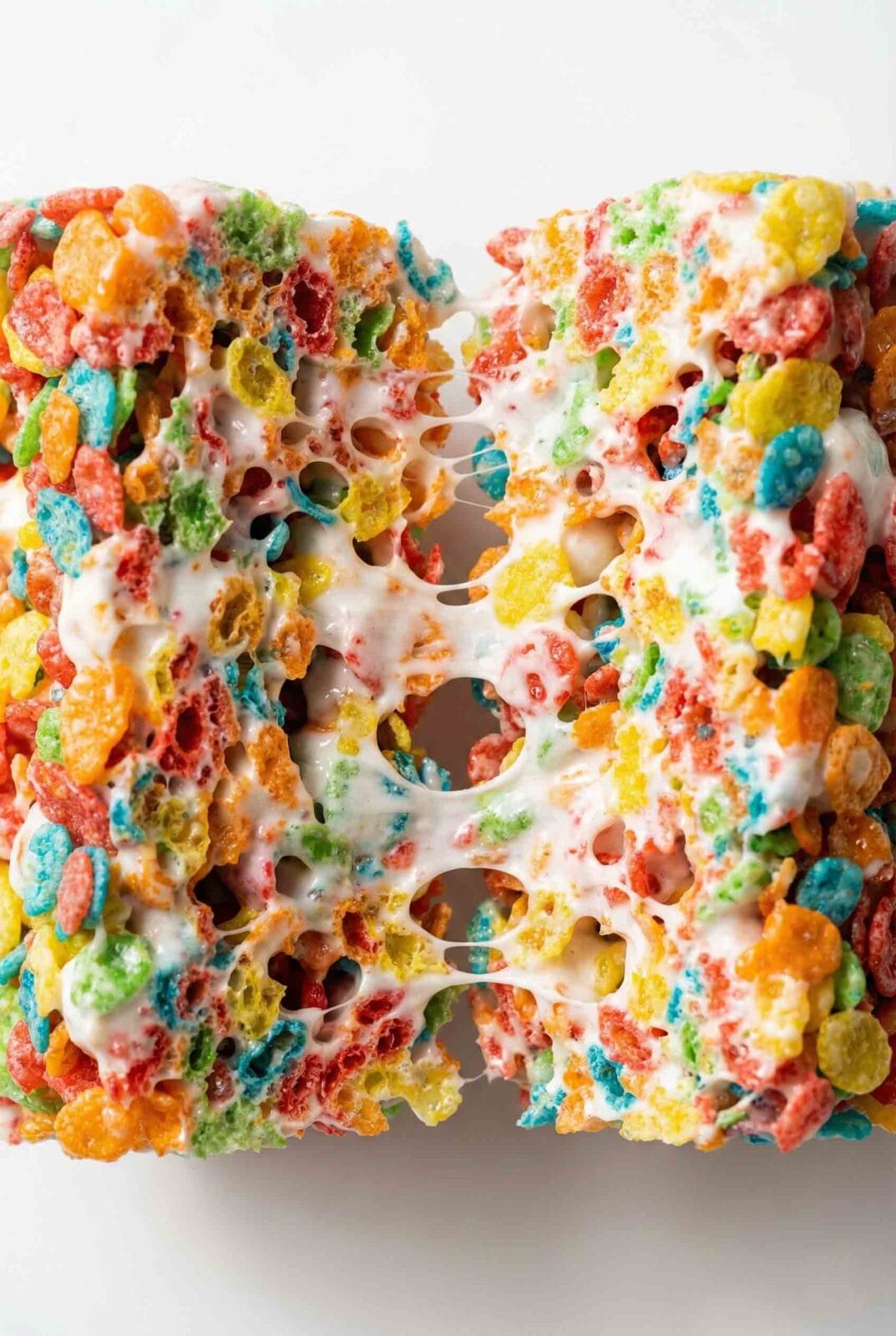 Fruity Pebbles Rice Krispie Treats pulled apart showing stretchy white marshmallow binding bright cereal pieces with soft chewy texture