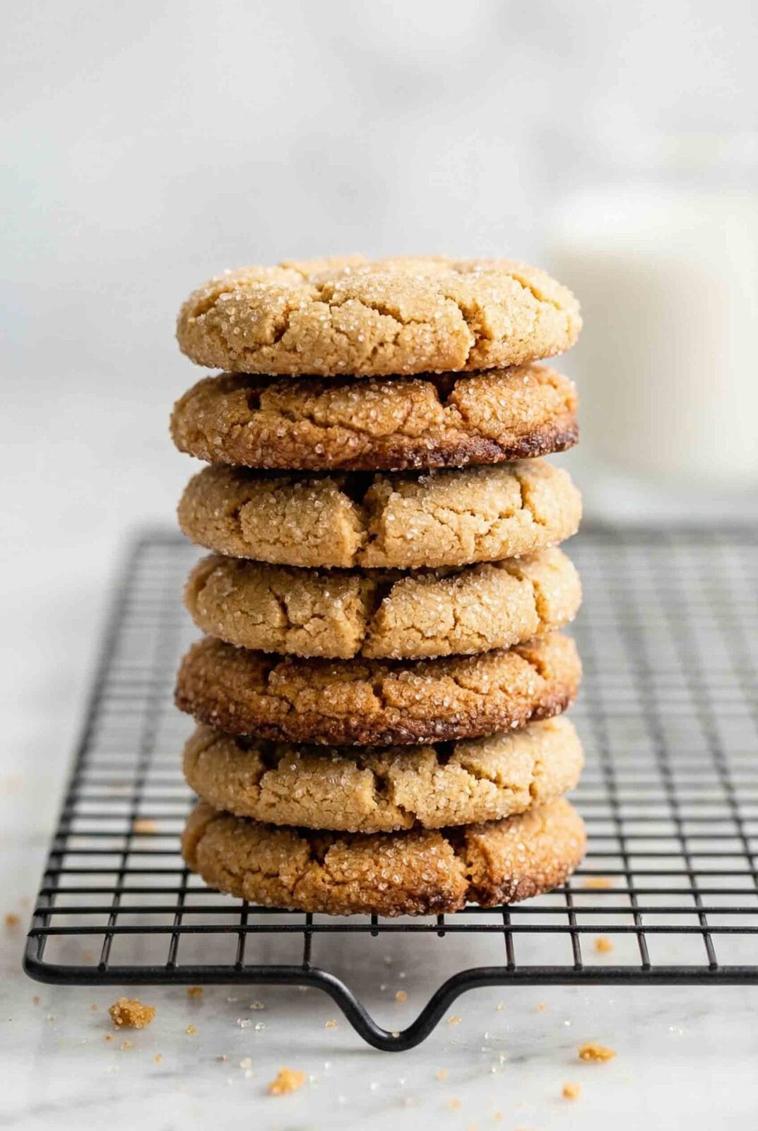 Stack of seven gluten-free peanut butter cookies on wire cooling rack showing crackled surface with coarse sugar coating and golden brown color with glass of milk in background