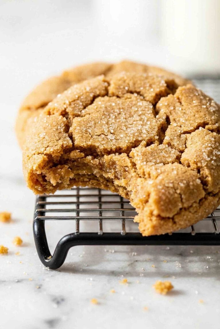 Close-up of gluten-free peanut butter cookie with bite taken showing soft chewy interior, crackled surface with sugar crystals on wire cooling rack on white surface