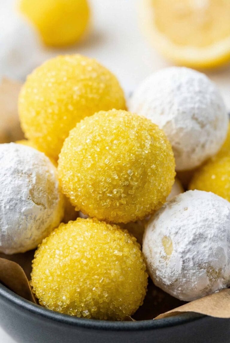 Extreme macro of lemon truffles clustered tightly, featuring bright yellow sanding sugar spheres and powdered sugar lemon truffles