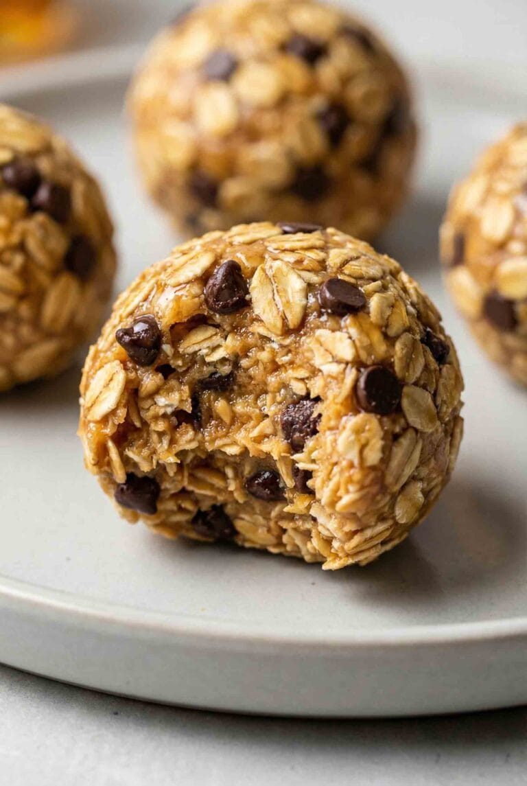 Macro close-up of a single oatmeal energy ball with a bite taken out, revealing a moist, chewy interior texture with oats and melted chocolate chips.