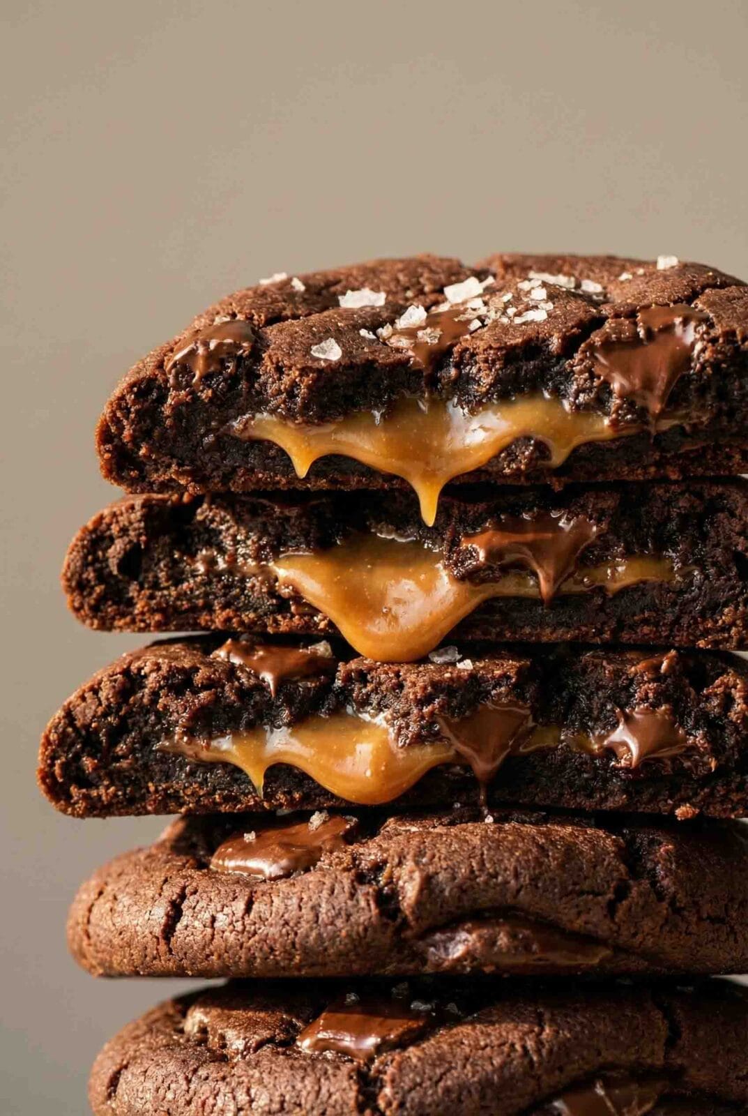Centered ultra-close stack of five salted caramel chocolate cookies with melted chocolate chunks, pressed caramel layers, and flaky sea salt