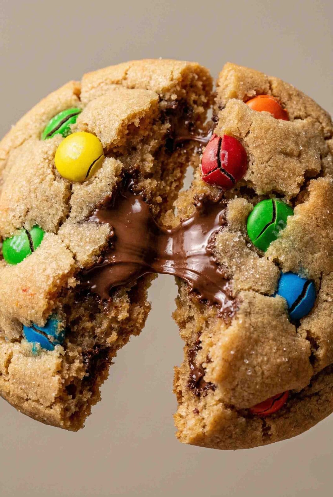 Extreme close-up of a soft M&M cookie broken open, showing gooey melted chocolate, colorful candy pieces, and a tender, chewy interior texture